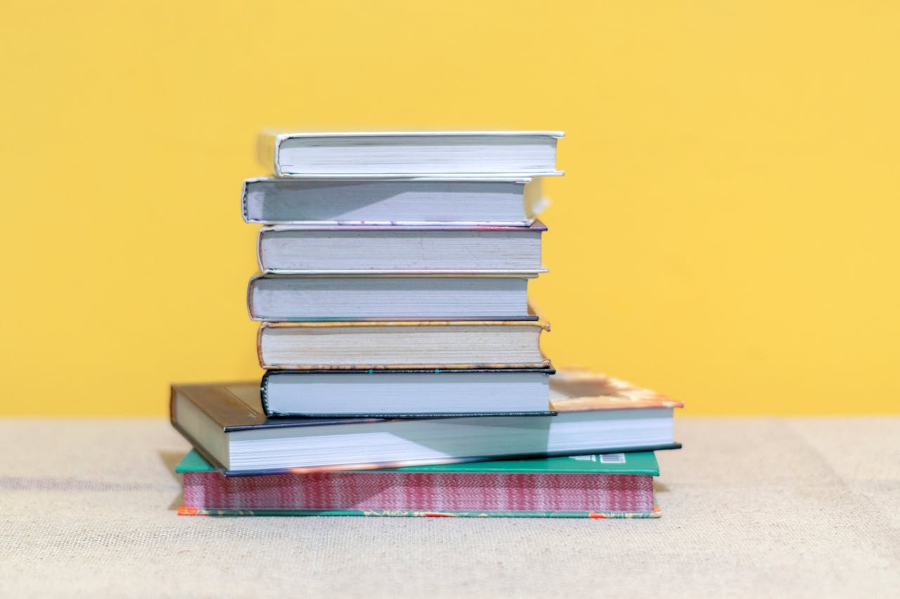 A stack of various books against a bright yellow background, ideal for education themes.